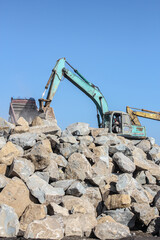 Obraz premium Yogyakarta August 20, 2011-Teal Excavator Moving Large Gray Rocks During Breakwater Construction Under Clear Blue Sky