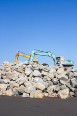 Obraz premium Yogyakarta August 20, 2011-Coastal Construction Site With Teal and Yellow Excavators on Rock Pile