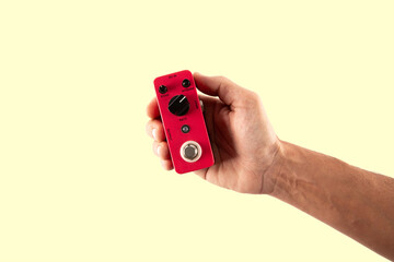 Male hand holding a pink guitar effects pedal isolated on light yellow background cutout
