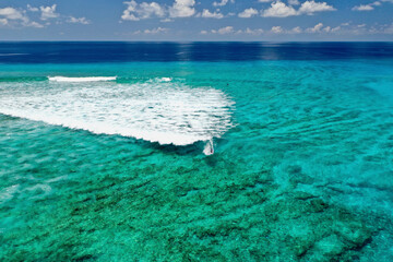 Aerial view of turquoise ocean waves and surfers at a beautiful beach, Maldives.