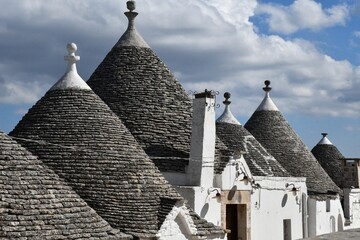 The grey stone and conical roofs of the trulli houses in Alberobello, with white stone wash walls. The sky is overcast with grey clouds.