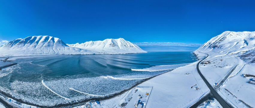 Aerial view of breathtaking winter landscape with snow-covered mountains and a serene lake, Troll Peninsula, Iceland.
