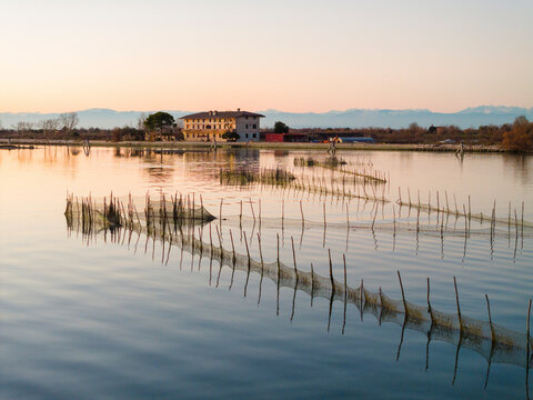 Aerial view of tranquil lagoon at sunset with serene reflections and fishing nets, Cavallino - Treporti, Italy.