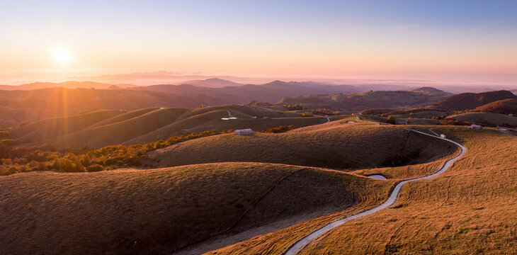Aerial view of serene rolling hills and a winding road at sunset, Rovere Veronese, Italy.