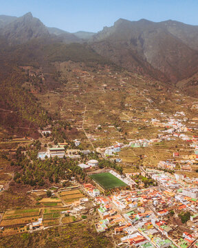 Aerial view of Estadio Municipal Blas Reyes surrounded by vibrant village and lush mountain landscape, Guimar, Spain.