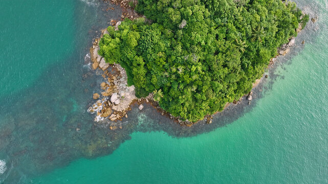 Aerial view of a beautiful tropical island surrounded by clear turquoise ocean and lush green forest, Ubatuba, Brazil.