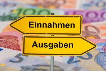 Zwei Wegweiser in gegensätzlicher Richtung sind beschriftet mit Einnahmen und Ausgaben -...