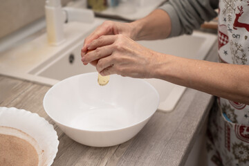 Woman cracking an egg into a bowl while making a traditional homemade dessert in the kitchen.