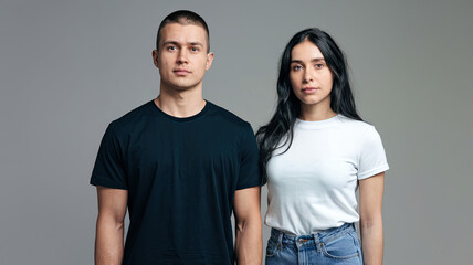 Fototapeta premium Casual Fashion Portrait of a Male in Black T-Shirt and a Female in White T-Shirt and Blue Jeans Standing Side by Side, Neutral Gray Background, Modern Stylish Look, High-Resolution Close-Up, Simple Cl