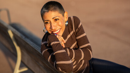 Woman smiling while leaning on a bench outdoors in sunlight