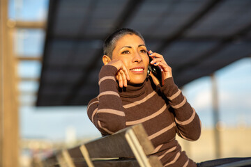 Woman talking on the phone and leaning on a wooden bench in natural light