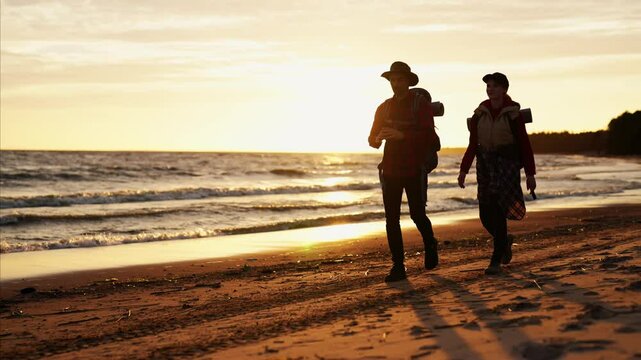 Traveling in nature, hikers admiring beautiful seascape in sunset, silhouette. People walking on coastline, enjoy freedom and beauty of nature, slow motion, cinematic shot with backers on seacoast