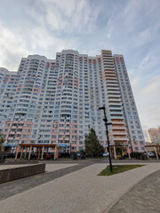 A large multi-story residential building with a pastel color palette of pink, white, and blue, featuring numerous balconies. The high-rise structure represents modern city living with an expansive