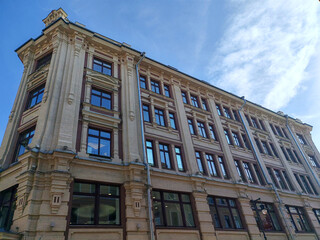 An elegant historic building with intricate brickwork and large windows reflecting the blue sky. The architectural grandeur suggests a story of urban development and hidden histories.