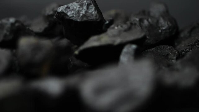 Coal chunks drop and collide in slow motion, breaking into smaller pieces. A macro study of this fossil fuel, beautifully lit for high-frame visuals.