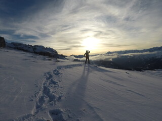 A breathtaking view of snowy mountains during sunset, with a hiker silhouetted against a glowing orange and blue sky.