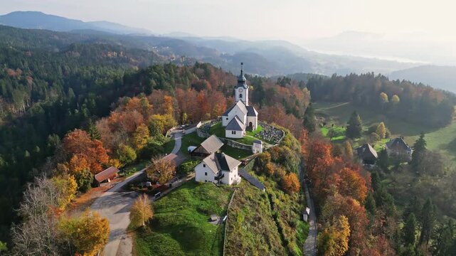 Aerial view of picturesque autumn landscape featuring a traditional church on a hill surrounded by serene forest and rural village, Sternberg, Velden am Woerthersee, Carinthia, Austria.