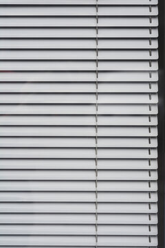 A close-up of closed white metal horizontal blinds, showcasing their parallel lines and subtle shadows