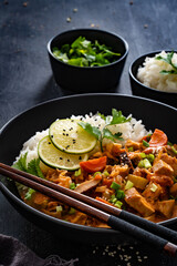 Thai food - chicken nuggets with vegetables, mushrooms and rice in tomato and coconut milk sauce on black table