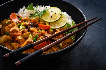 Thai food - chicken nuggets with vegetables, mushrooms and rice in tomato and coconut milk sauce on black table