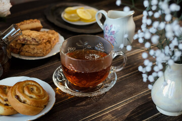 Tea party, morning breakfast. Transparent cup of tea and fresh pastries on kitchen table. 