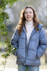Young woman wearing blue puffer jacket is posing near green leaves