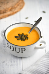 Pumpkin creamy soup served in bowl. High angle view of soup in bowl on white wooden table