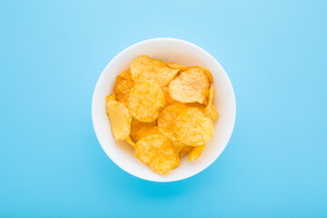 Full white bowl of yellow potato chips on light blue table background. Pastel color. Closeup. Top down view. © fotoduets