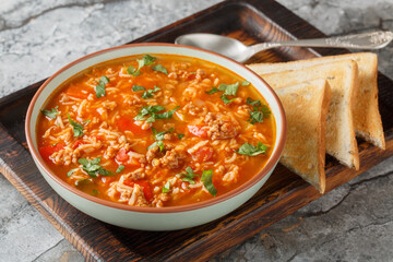 Hot stuffed pepper soup is a hearty meal loaded with ground beef, onions, rice and bell peppers in a tomato based broth closeup in the bowl on the table. Horizontal