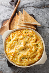 Twice baked mashed potatoes are light and fluffy with butter, cheese closeup on the baking dish on the table. Vertical top view from above