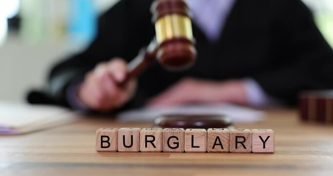 Professional judge strikes gavel to declare accused guilty of burglary. Miniature wooden blocks form word BURGLARY on table. Slow motion