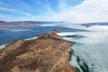 Stunning aerial view of the frozen lake in spring, surrounded by hills, cozy bays where tourist houses and camp sites are located. Ice melting time.