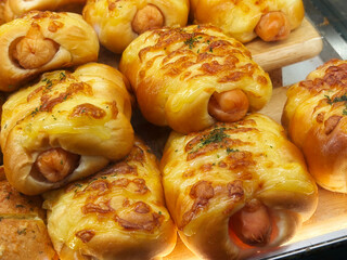 Close-up Thai-style sausage buns on a wooden shelf in a bakery store, warm light from the top. Stack of sausage bun.