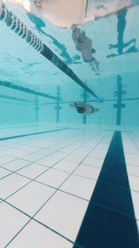 Professional swimmer works out underwater in a public pool and trains freediving no fins discipline, DNF, dynamic no fins
