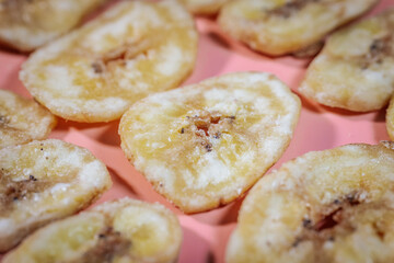 A close-up of freeze-dried banana chips arranged on a pink surface, highlighting their golden yellow color and crunchy texture. Perfect for food, snacks, and healthy eating themes.
