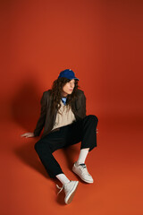 Stylish young man seated against a vibrant orange backdrop showcasing modern fashion trends