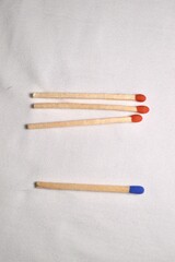 A single blue match and three red matches arranged neatly against a white fabric backdrop.