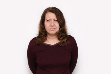 Obraz premium A serious woman wearing a maroon top is standing against a white gradient background. Her expression conveys determination, thoughtfulness, resilience. A little sad middle aged woman