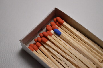 A lone blue matchstick contrasts beautifully among a sea of orange in its matchbox.