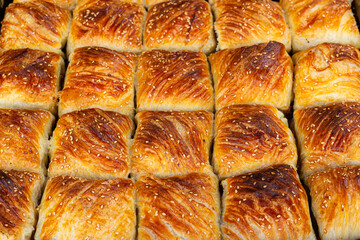 Background from tasty freshly baked samsa with sesame kernels, Uzbekistan. Samosa is a popular savoury pastry in Central Asian cuisines. It represents a puff bun stuffed with meat or vegetables