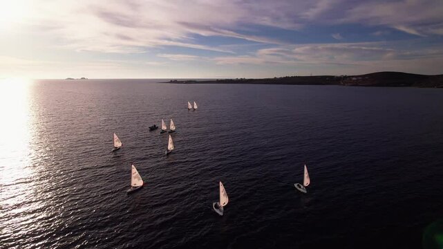 Drone shot of sail&iota;ng boats with sails outside of Parikia town on Paros island in Greece. Drone flying towards them.