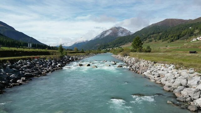 Aerial view of serene river inn surrounded by majestic mountains and lush greenery, Zuoz, Switzerland.
