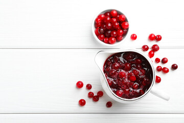 Tasty cranberry sauce in gravy boat and berries on white wooden table, top view. Space for text
