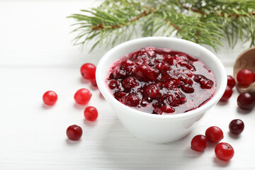 Tasty cranberry sauce in bowl, berries and fir tree branches on white wooden table, closeup
