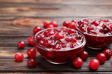 Tasty cranberry sauce in glass bowls and berries on wooden table, closeup