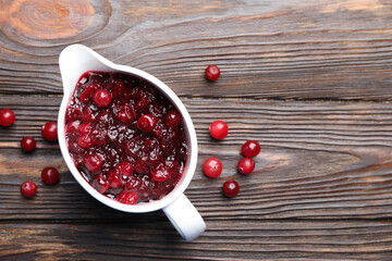 Tasty cranberry sauce in gravy boat and berries on wooden table, top view. Space for text