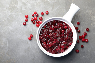 Tasty cranberry sauce in gravy boat and berries on grey table, top view. Space for text