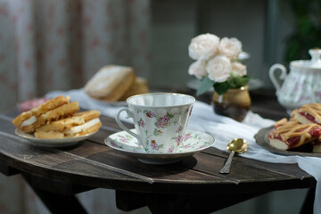 Porcelain tea cup and baked goods on table. Kitchen table is set for tea drinking.