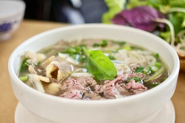 
A bowl of rare beef pho with a basket of fresh herbs and bean sprouts at Phu Quoc, a Vietnamese Chinese restaurant in Cabramatta - Sydney, NSW, Australia 