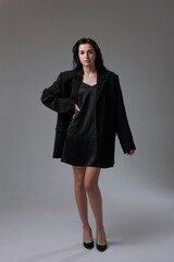 Fashion portrait of a confident model wearing oversized blazer and black dress in a minimalist...